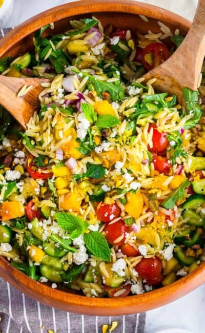 Colorful summer orzo salad with peaches, cherry tomatoes, cucumbers, and feta served in a large white bowl.
