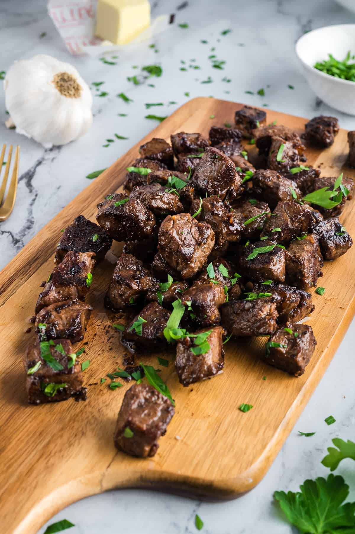 Steak bites garnished with parsley on a cutting board. 