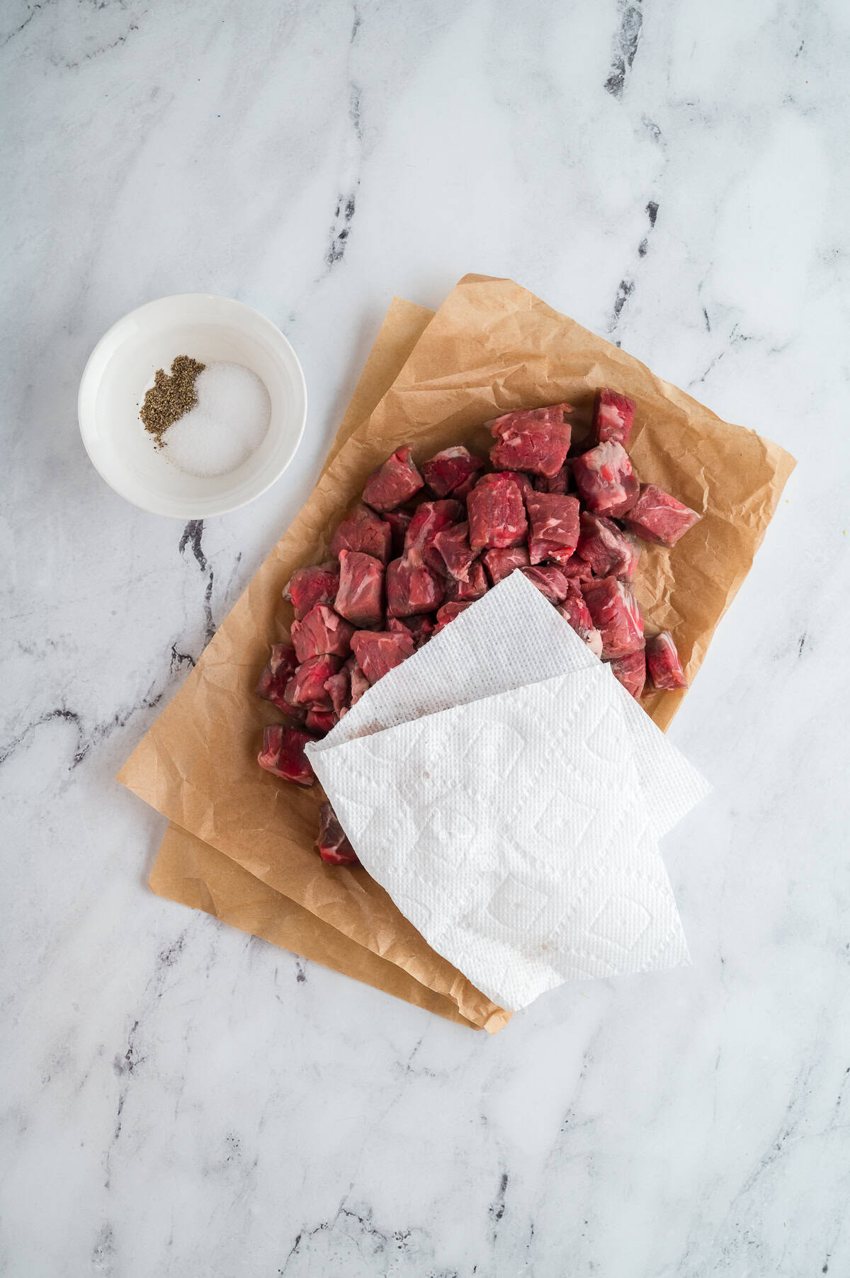 Steak cut into bite sized pieces on butcher paper and being dried with a paper towel. 