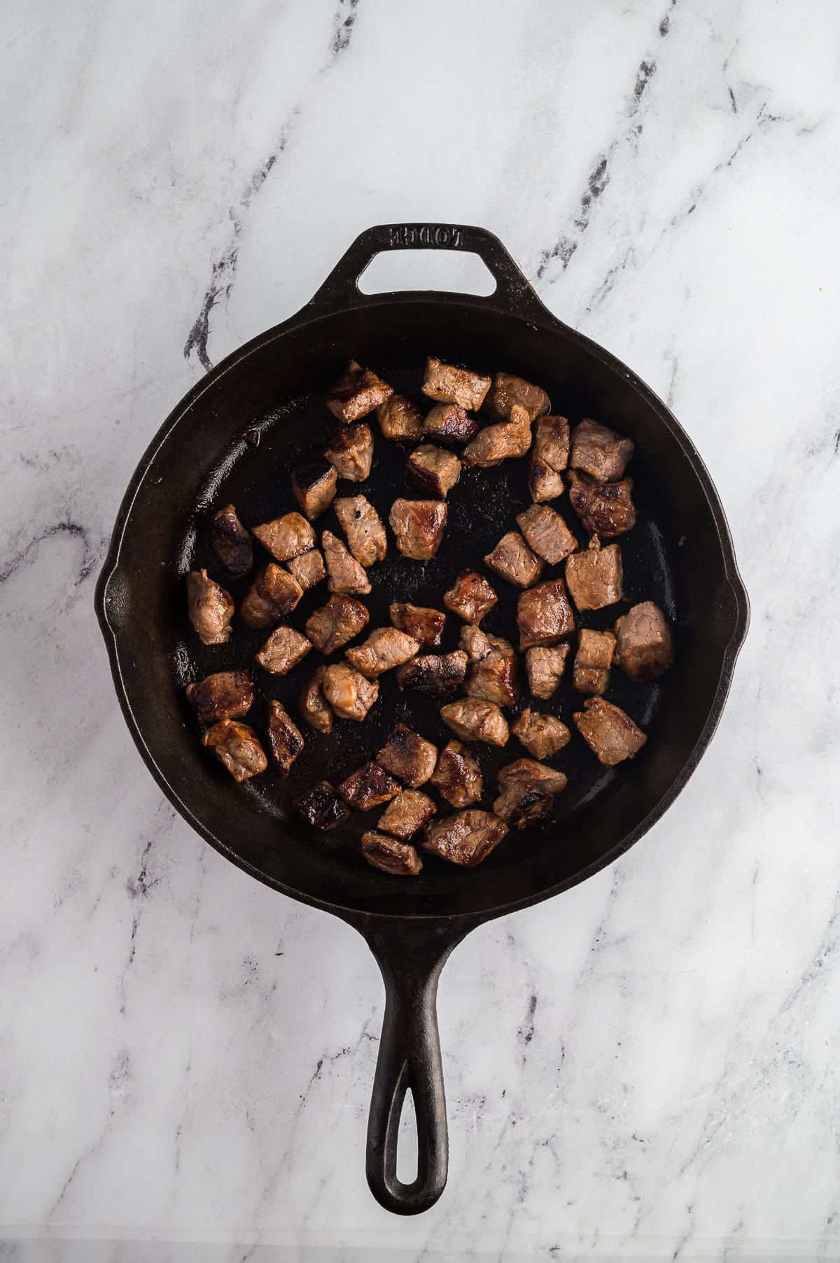 Steak bites being seared in a cast-iron pan. 