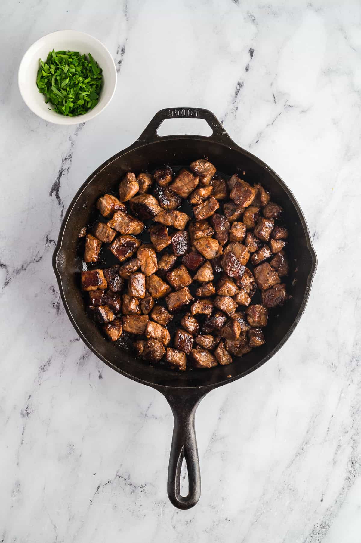 Steak bites coated in a buttery garlic sauce in a cast iron pan.  
