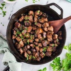 Cast-iron skillet with garlic butter steak bites garnished with fresh parsely.