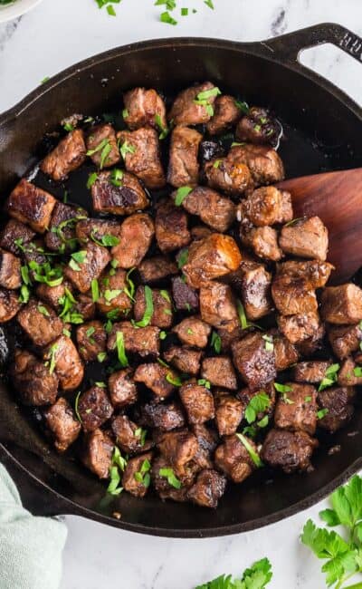 Cast-iron skillet with garlic butter steak bites garnished with fresh parsely.