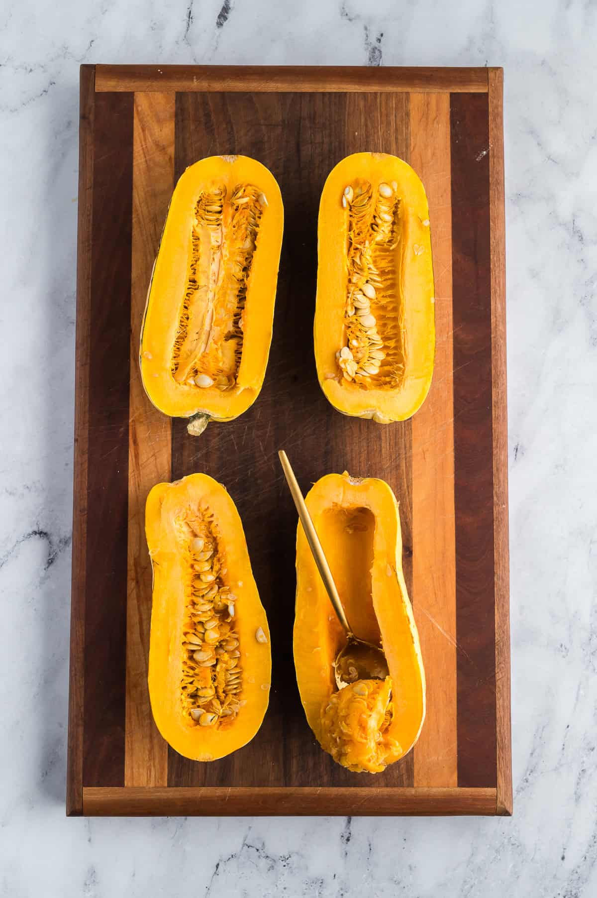 A spoon scooping seeds out of the center of a half of squash.