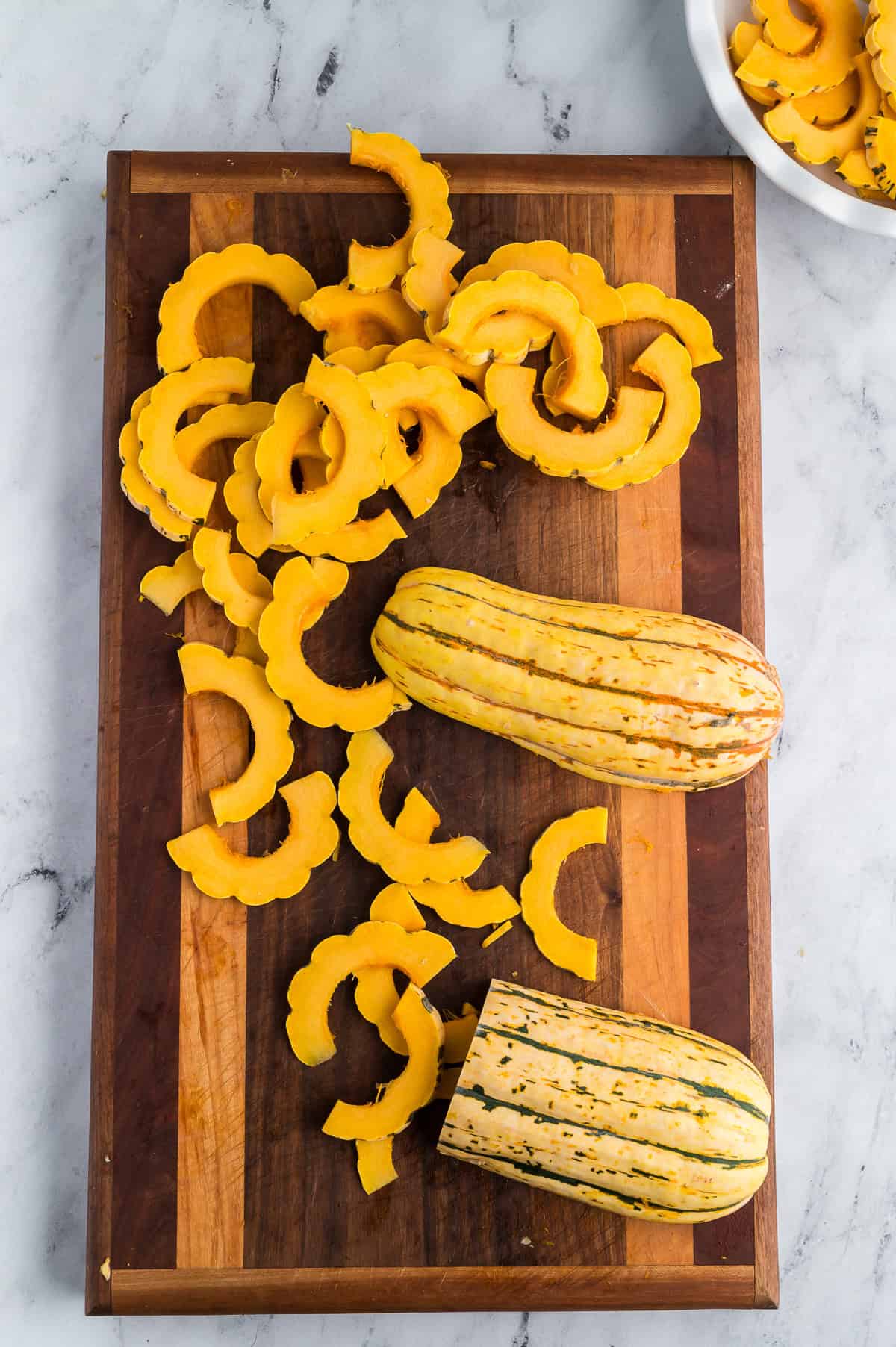 Sliced delicata squash on a wooden cutting board.