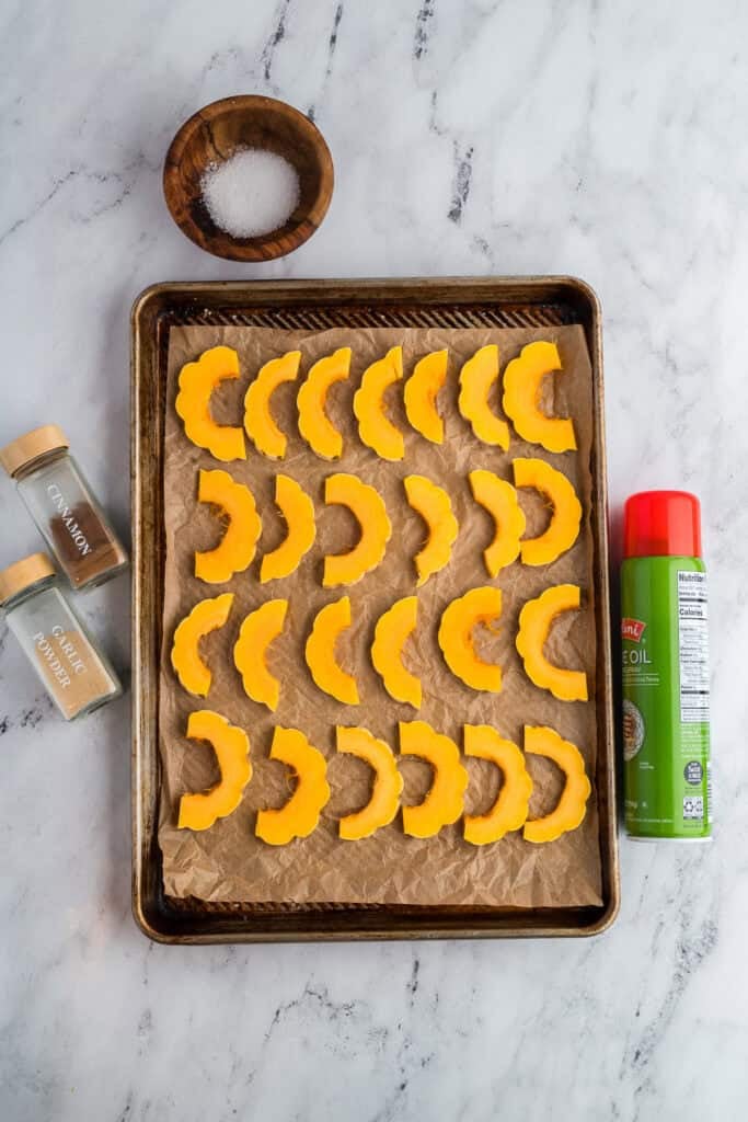 Sliced delicata squash on a baking sheet with seasonings around it.