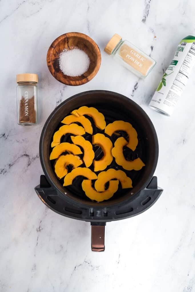 Sliced delicata squash and ingredients around an air fryer.