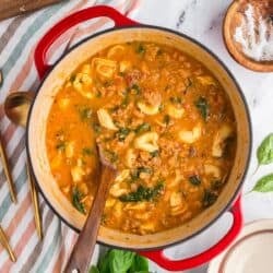 Creamy tortellini soup with chicken sausage and spinach in a red dutch oven.