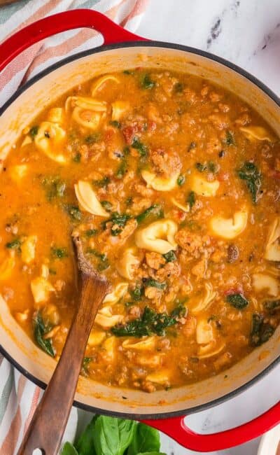 Creamy tortellini soup with chicken sausage and spinach in a red dutch oven.