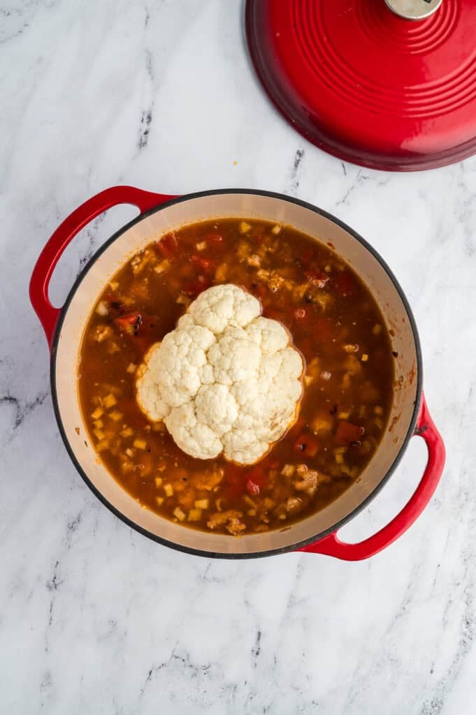 A small head of cauliflower in a pot of soup.