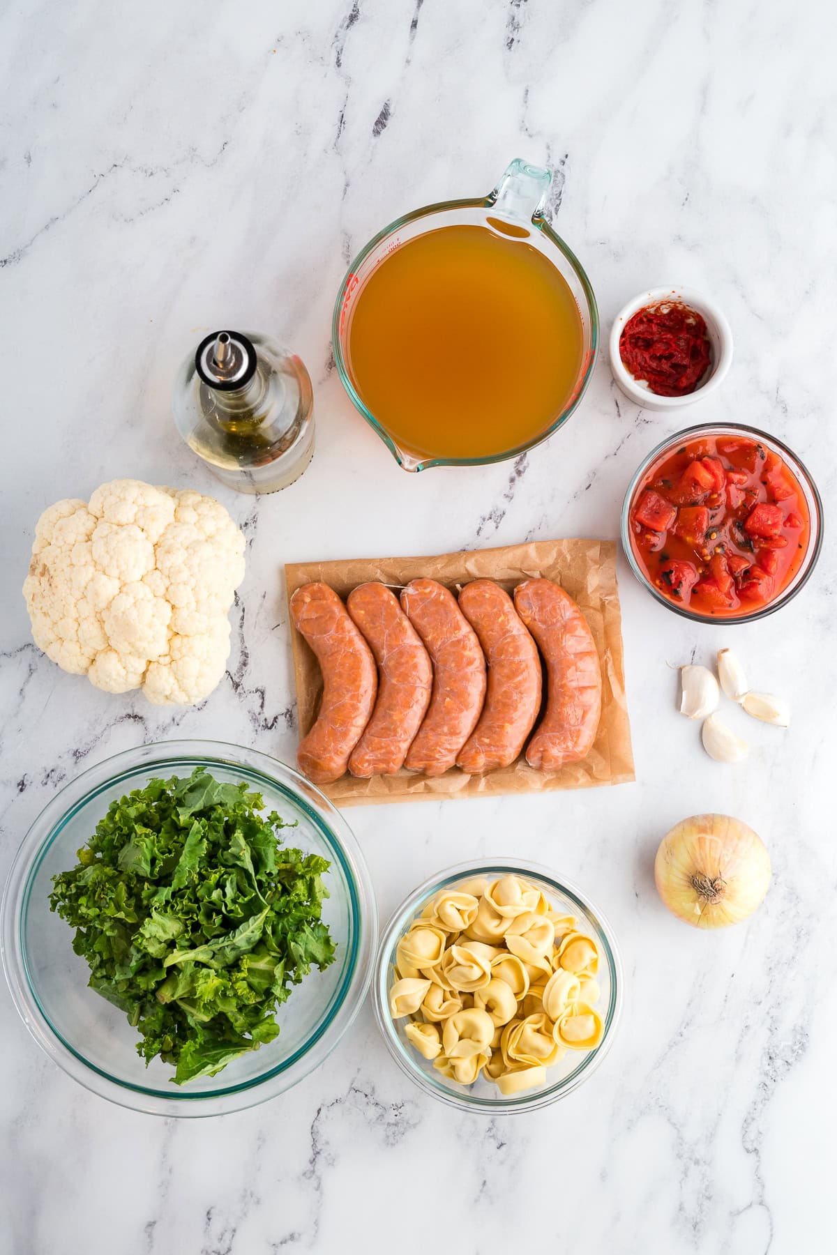 Ingredients for soup - gluten free tortellini, chicken sausage, broth, kale, onion, garlic, tomatoes and cauliflower.