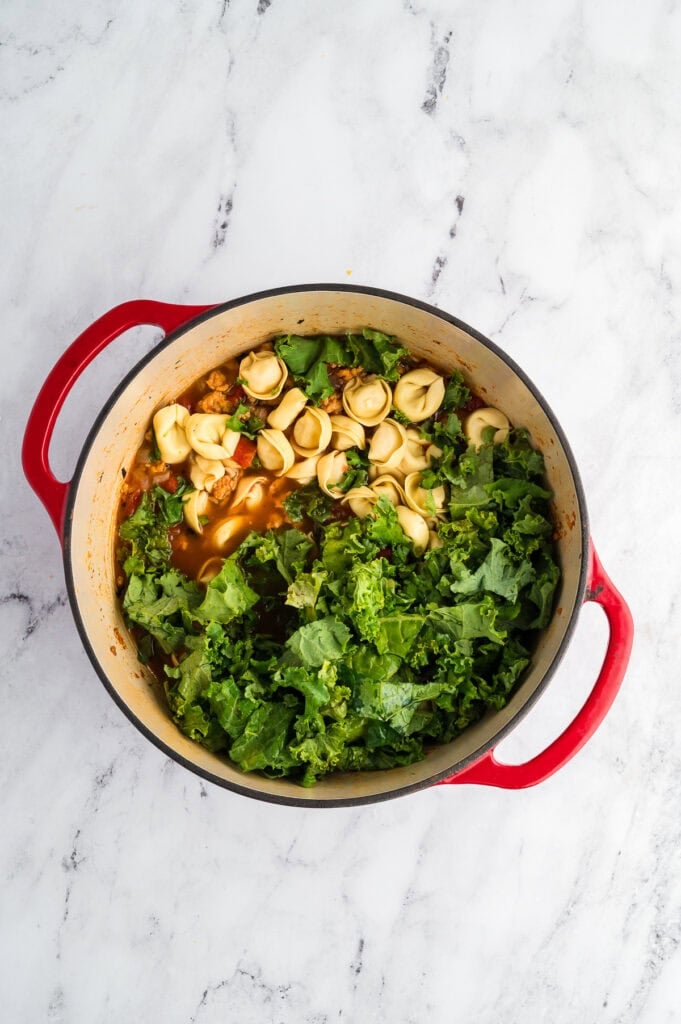 A pot of soup with tortellini and kale.