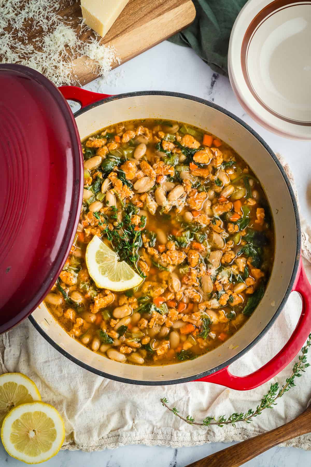 Hearty Tuscan-style white bean soup with sausage and vegetables served in a Dutch oven with lemon wedges and fresh herbs on top.