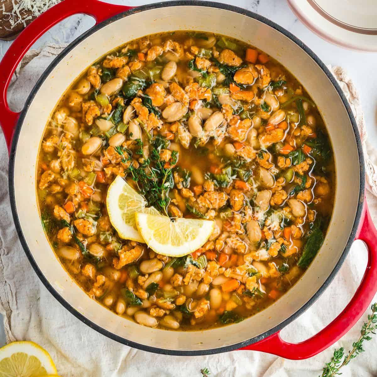 Hearty Tuscan-style white bean soup with kale and vegetables served in a Dutch oven with lemon wedges on top.