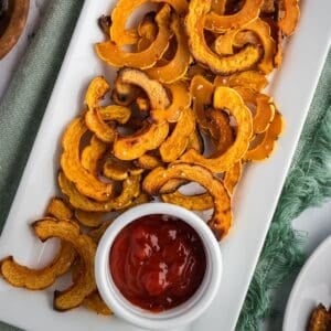 Crispy roasted delicata squash on a white platter with a small ramekin of ketchup.