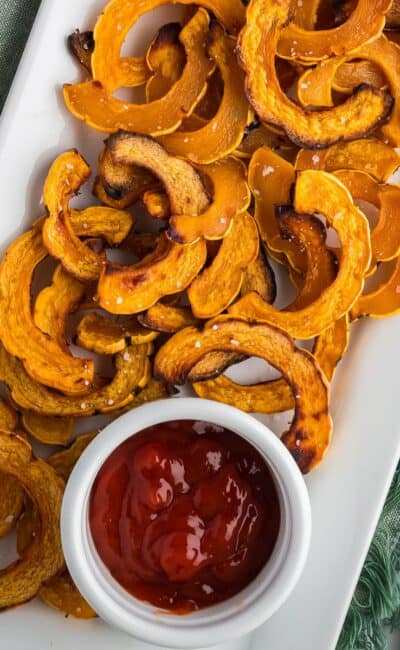 Crispy roasted delicata squash on a white platter with a small ramekin of ketchup.