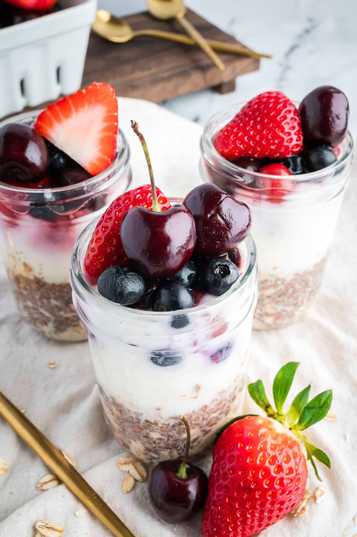 Overhead view of three jars of overnight oats layered with oats, yogurt, and frozen mixed berries.