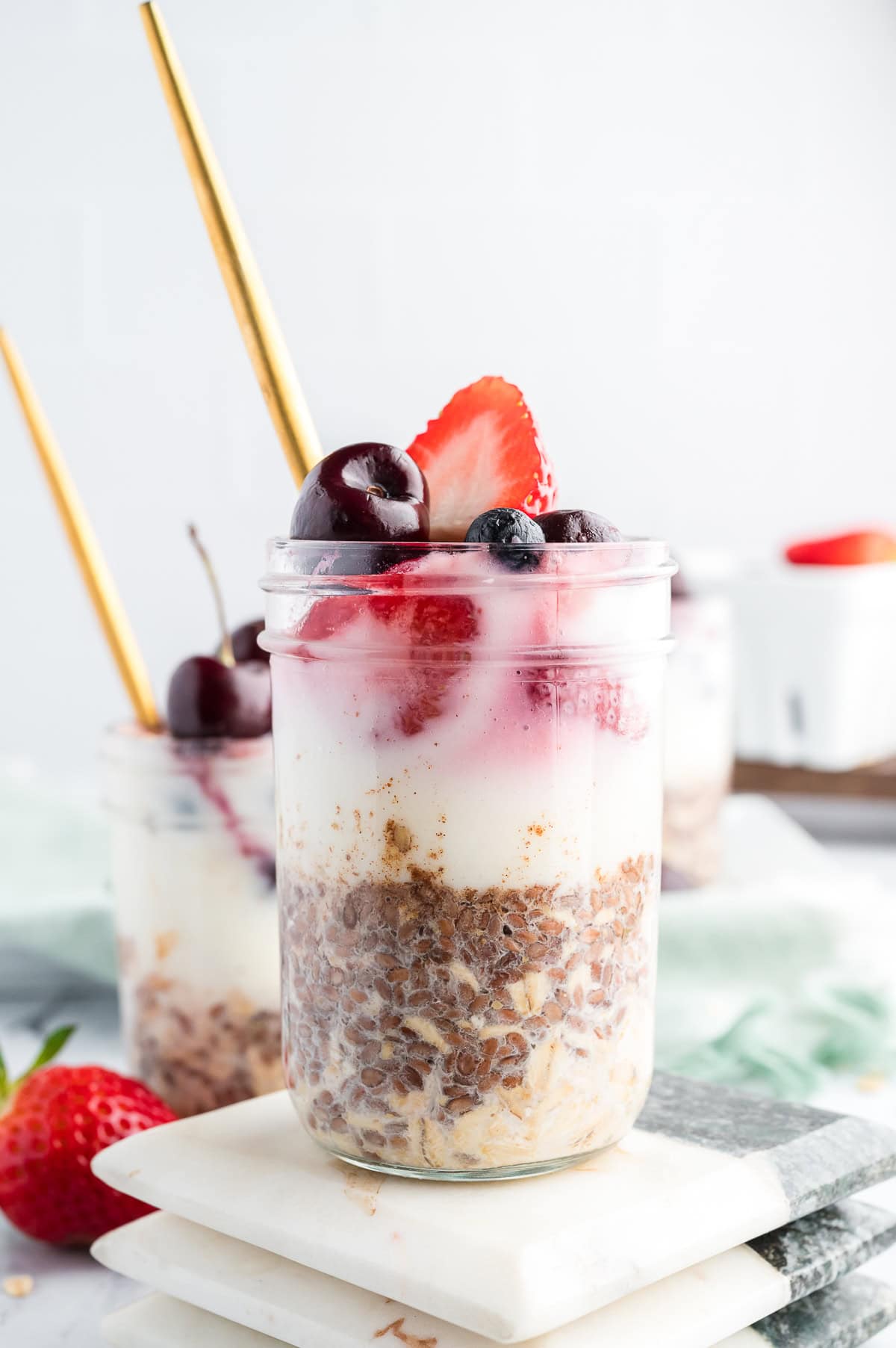 High-protein overnight oats in glass jars layered with oats, yogurt, and berries, styled with gold spoons.