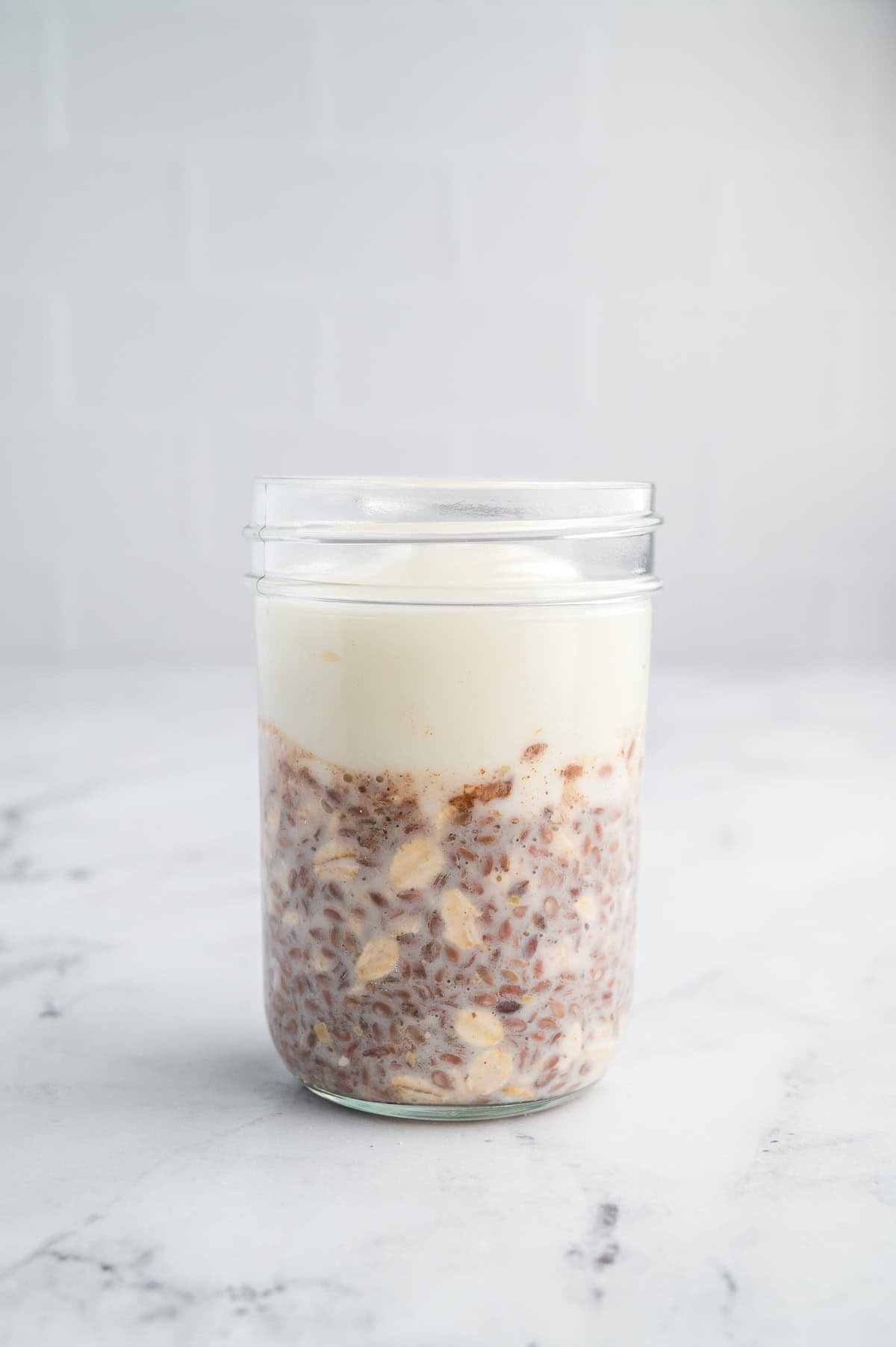 Glass jar of high-protein overnight oats layered with oats and Greek yogurt on a white marble surface.
