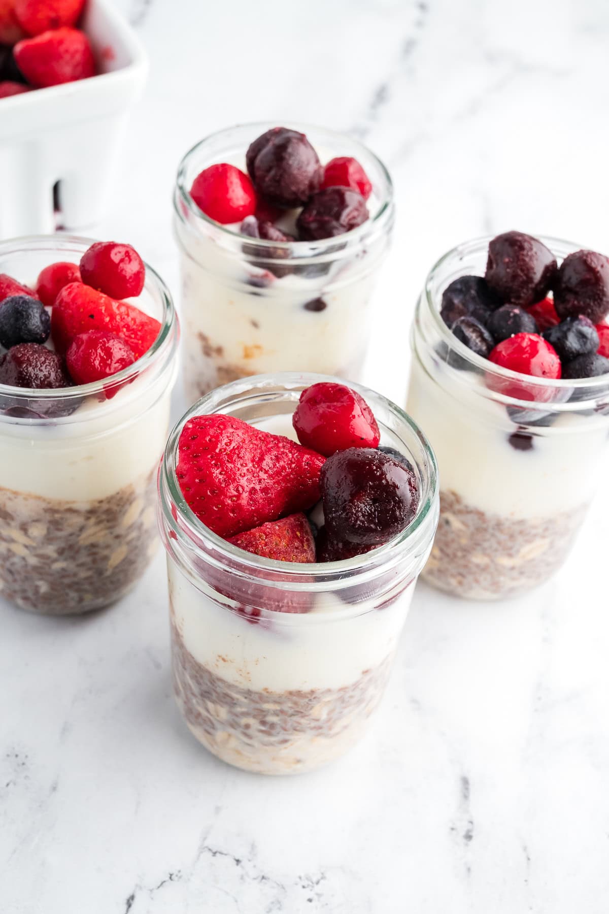 Overhead view of four jars of overnight oats layered with oats, yogurt, and frozen mixed berries.