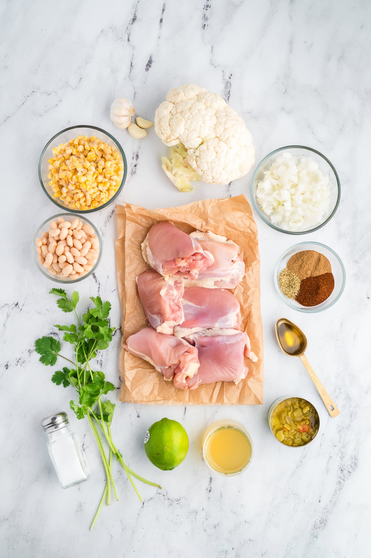 Ingredients for white chicken chili including raw chicken, cauliflower, white beans, corn, onion, spices, garlic, lime, and cilantro.