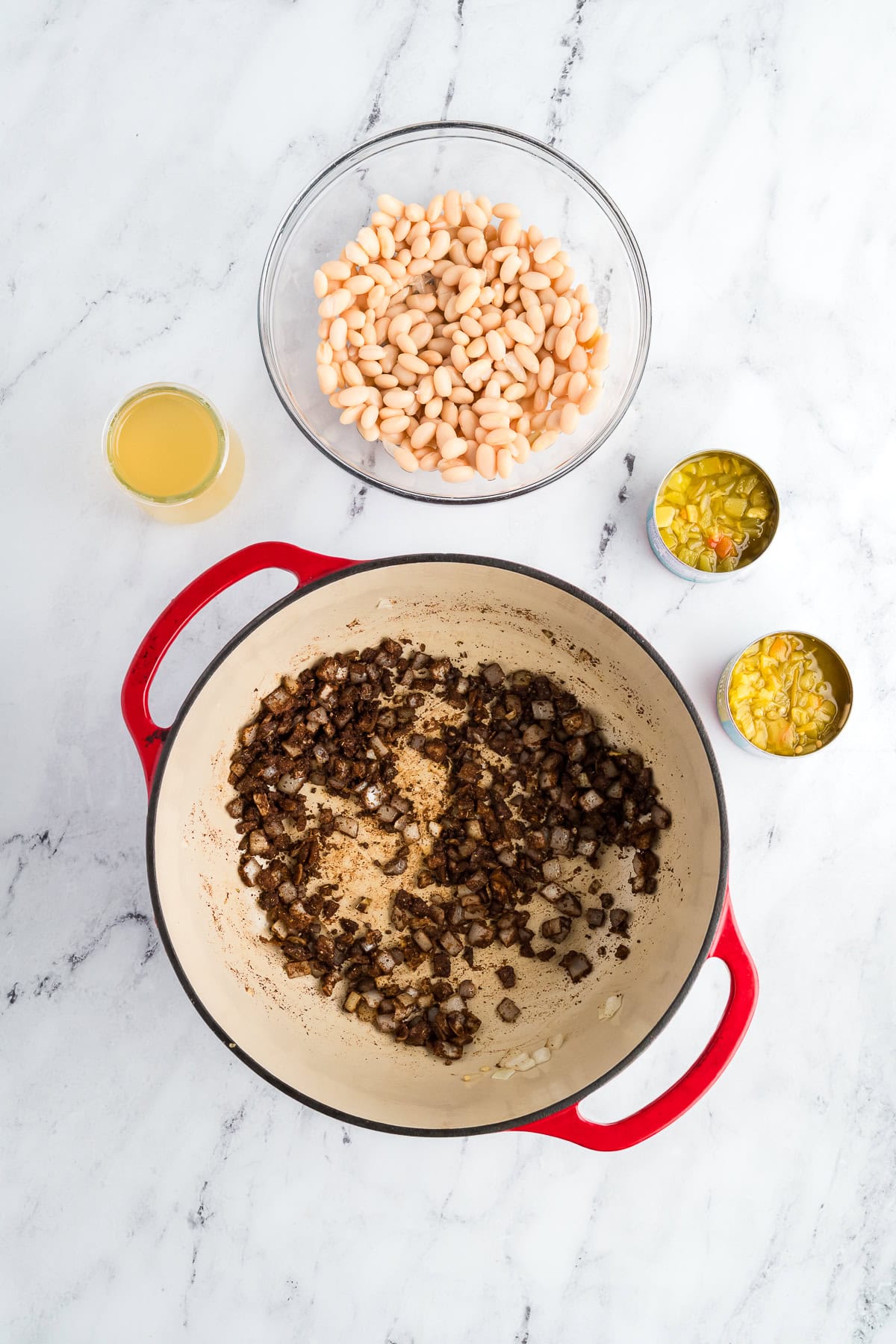 Diced onions sautéing with spices in a red Dutch oven, building flavor for white chicken chili.